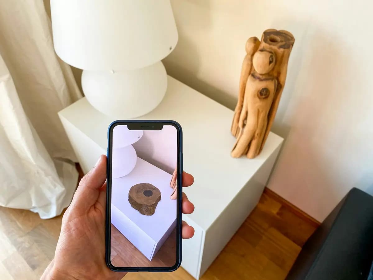 A hand holding a phone that shows a 3D object placed on a table through the camera
